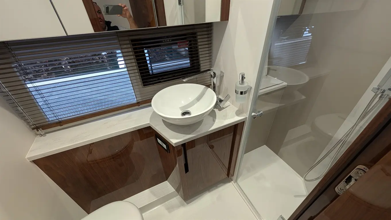Modern bathroom featuring a washbasin, mirror, and shower enclosure with glass door, natural light from window blinds.